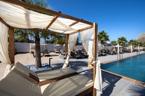 A poolside area with sun loungers, a wooden pergola with white fabric, and palm trees. - Paradice Hotel Luxury Suites (Chania)