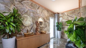 A marble-floored bathroom with a wooden vanity, a bronze statue, and large potted plants. - Paradice Hotel Luxury Suites (Chania)