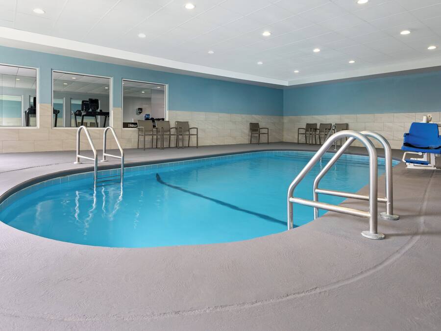 An indoor swimming pool with clear blue water, metal ladders, and a blue lifeguard chair.