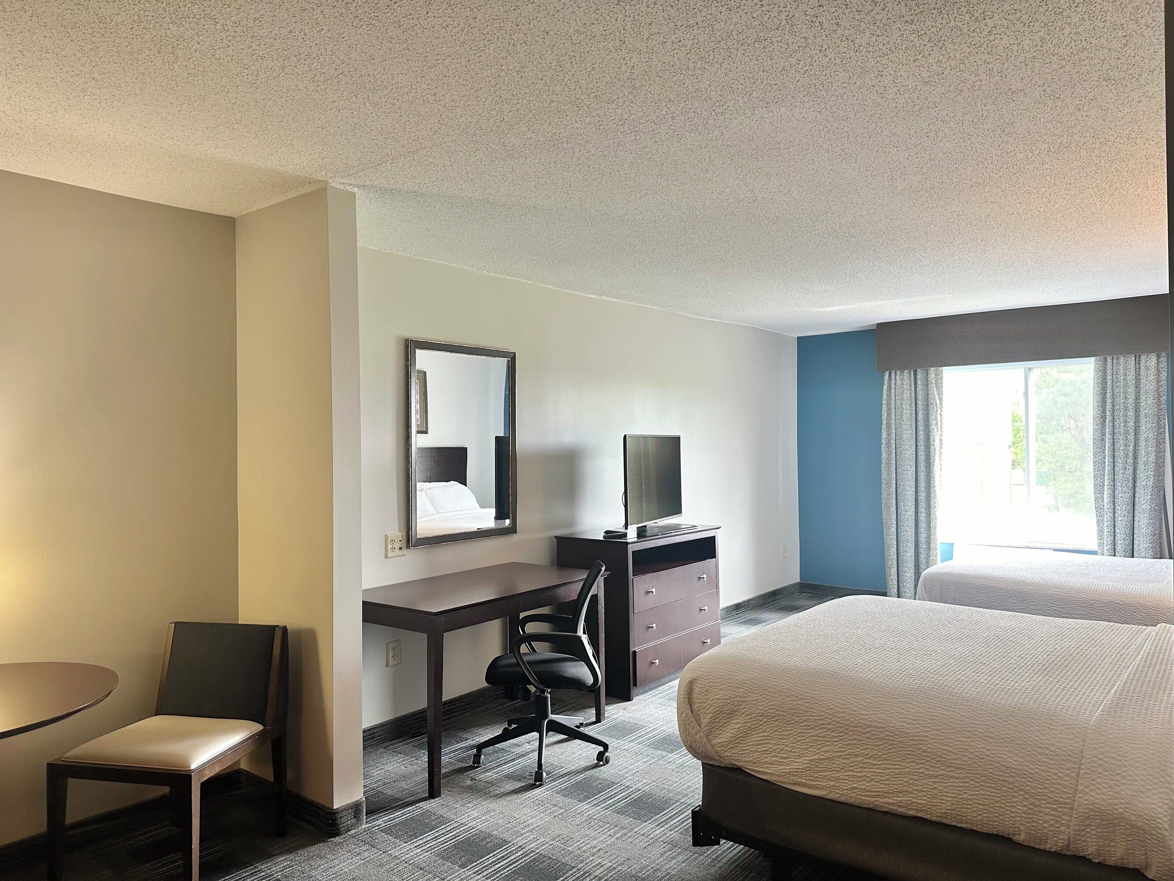 A hotel room with a bed, a desk with a chair, a television, and a window with curtains.