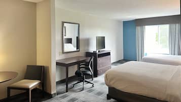 A hotel room with a bed, a desk with a chair, a television, and a window with curtains.
