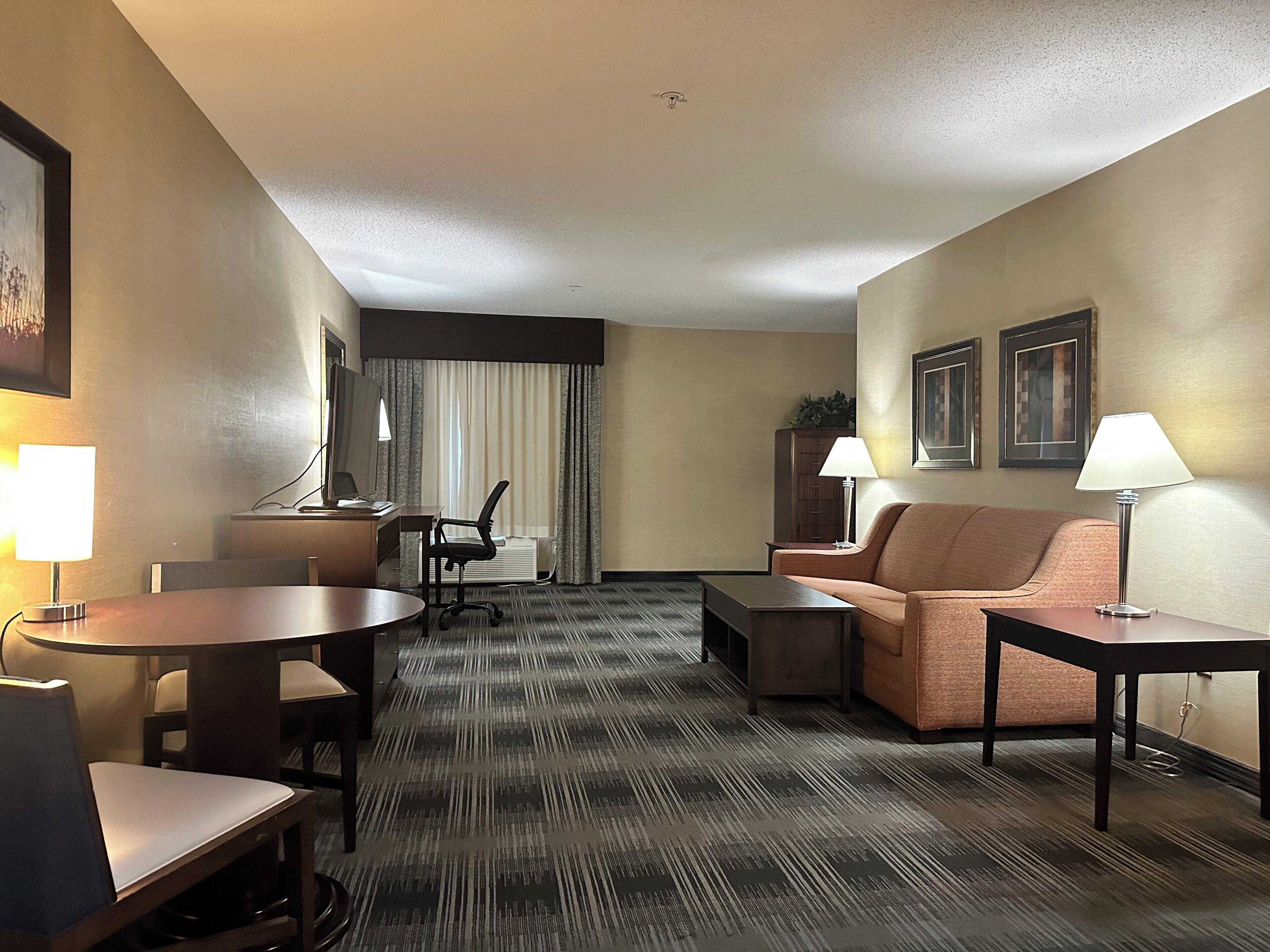A hotel room with a desk, chair, sofa, and two lamps.