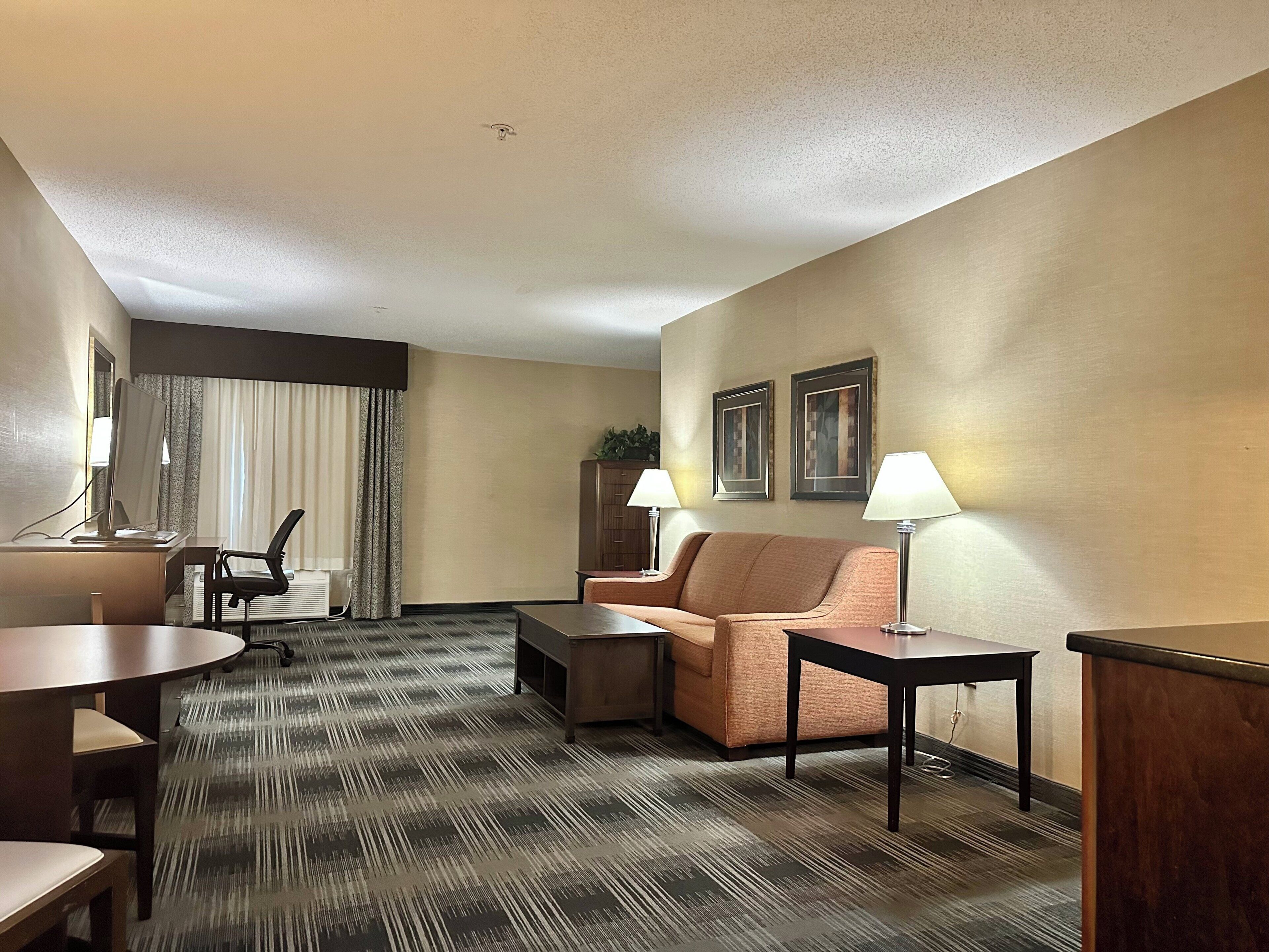 A hotel room with a sofa, a desk with a computer, a small table, and two lamps.