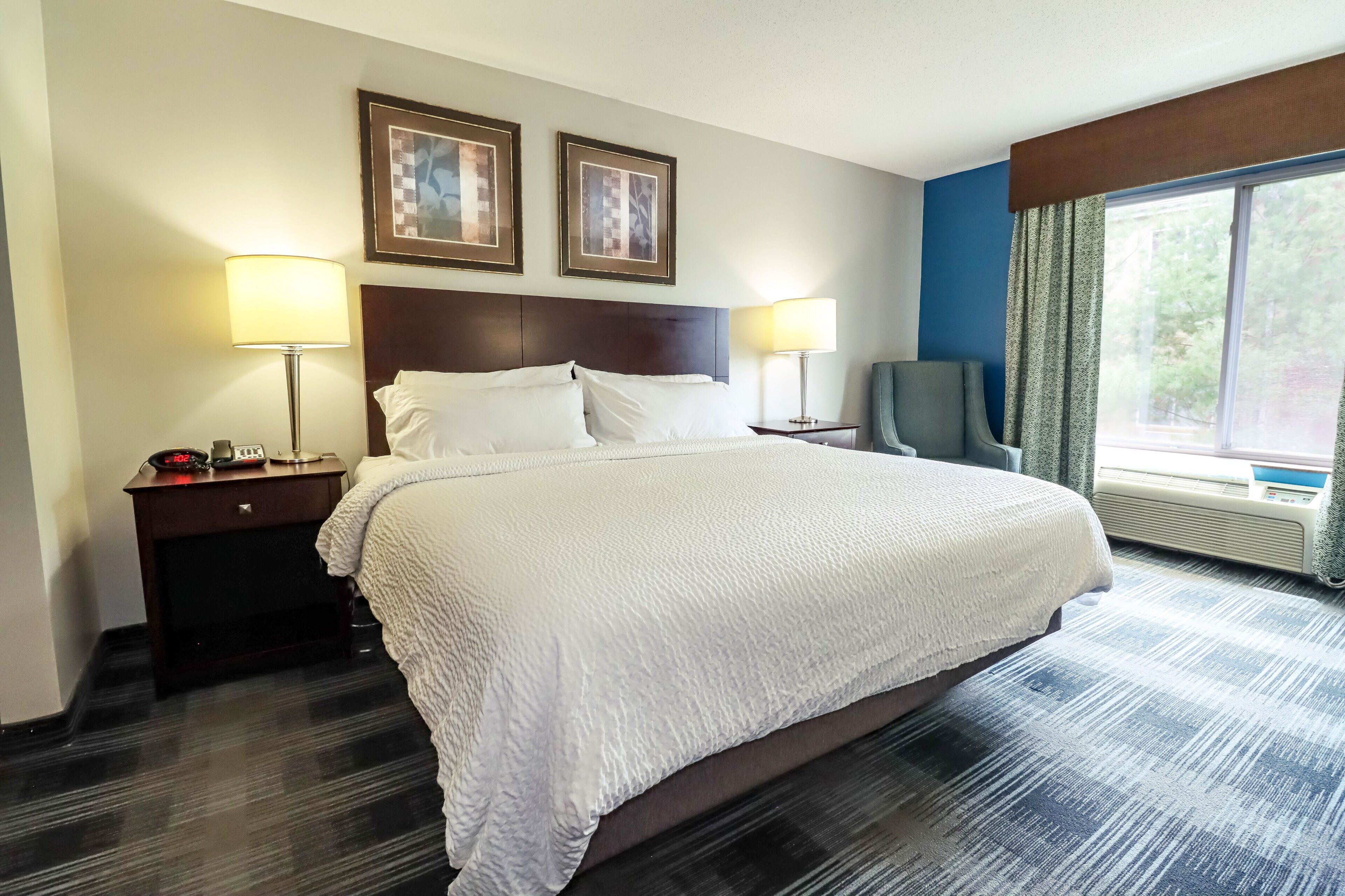 Een hotelkamer met een groot bed, twee bedlampen, een nachtkastje met een telefoon, een stoel en een raam met gordijnen.