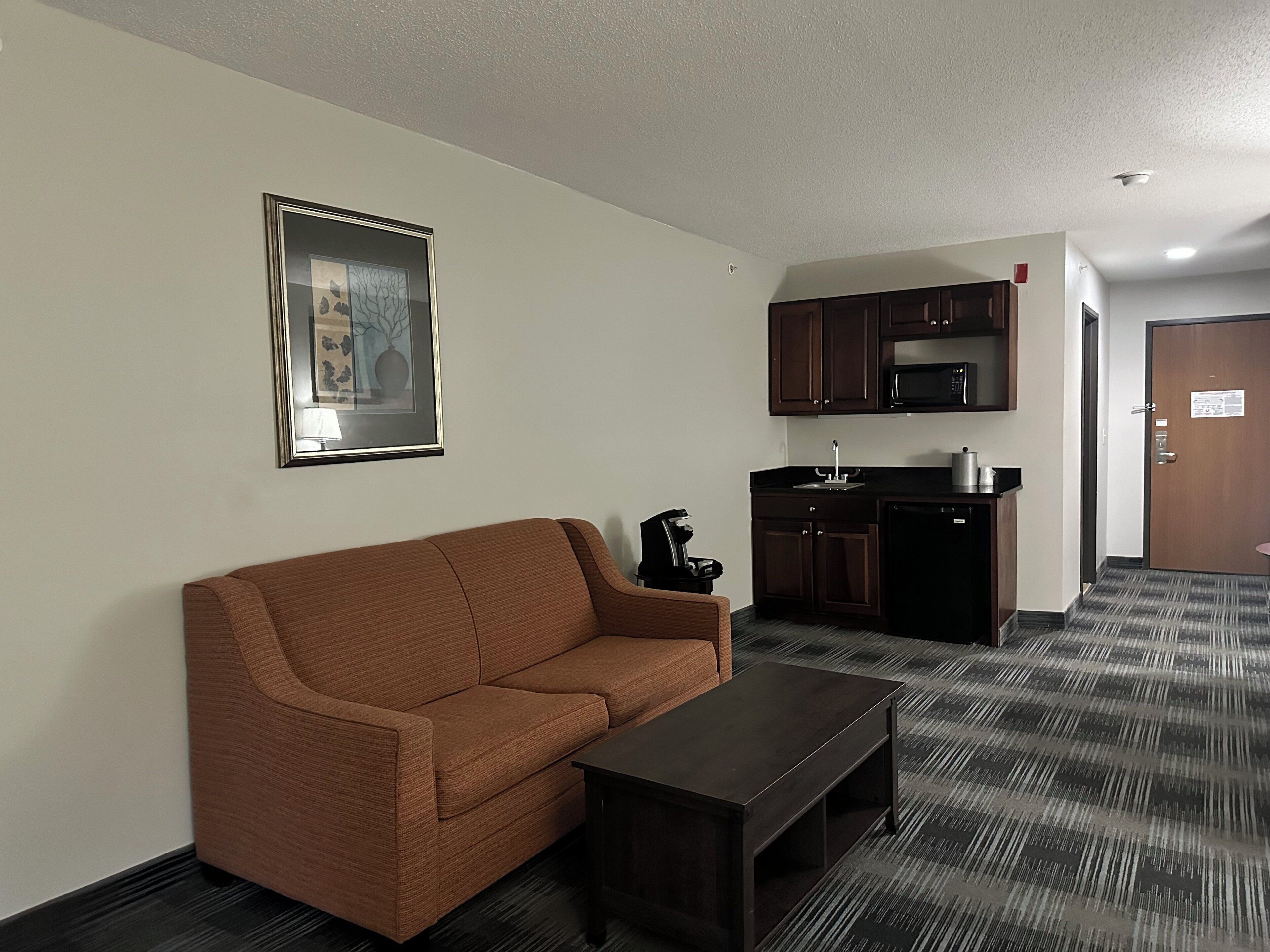 A living area with a sofa, coffee table, kitchenette, and a door.