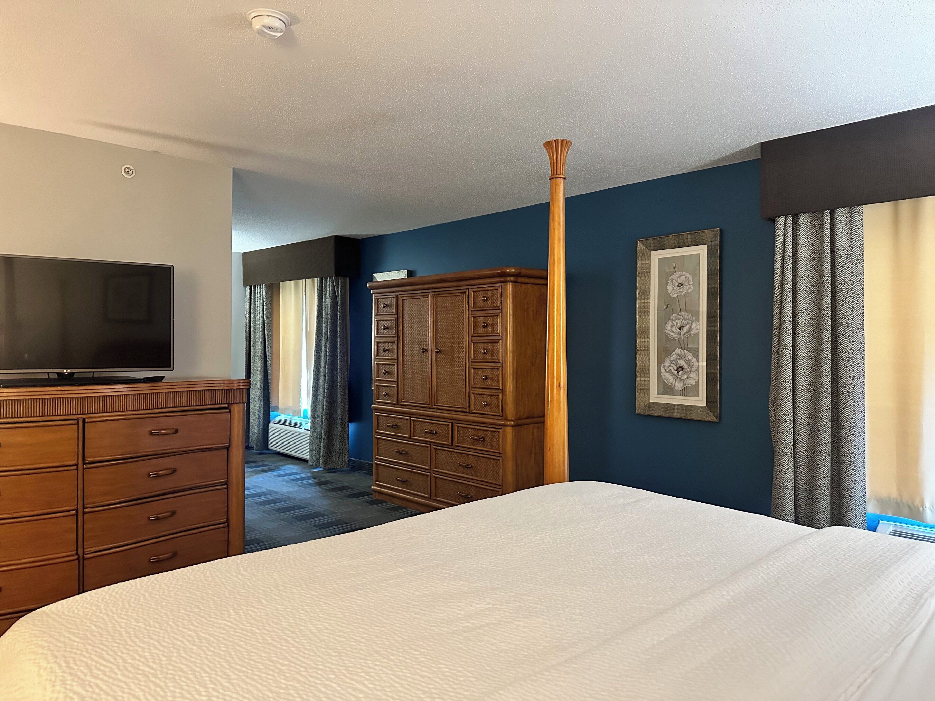 A hotel room with a bed, a dresser, a television, a wardrobe, and a framed picture on the wall.