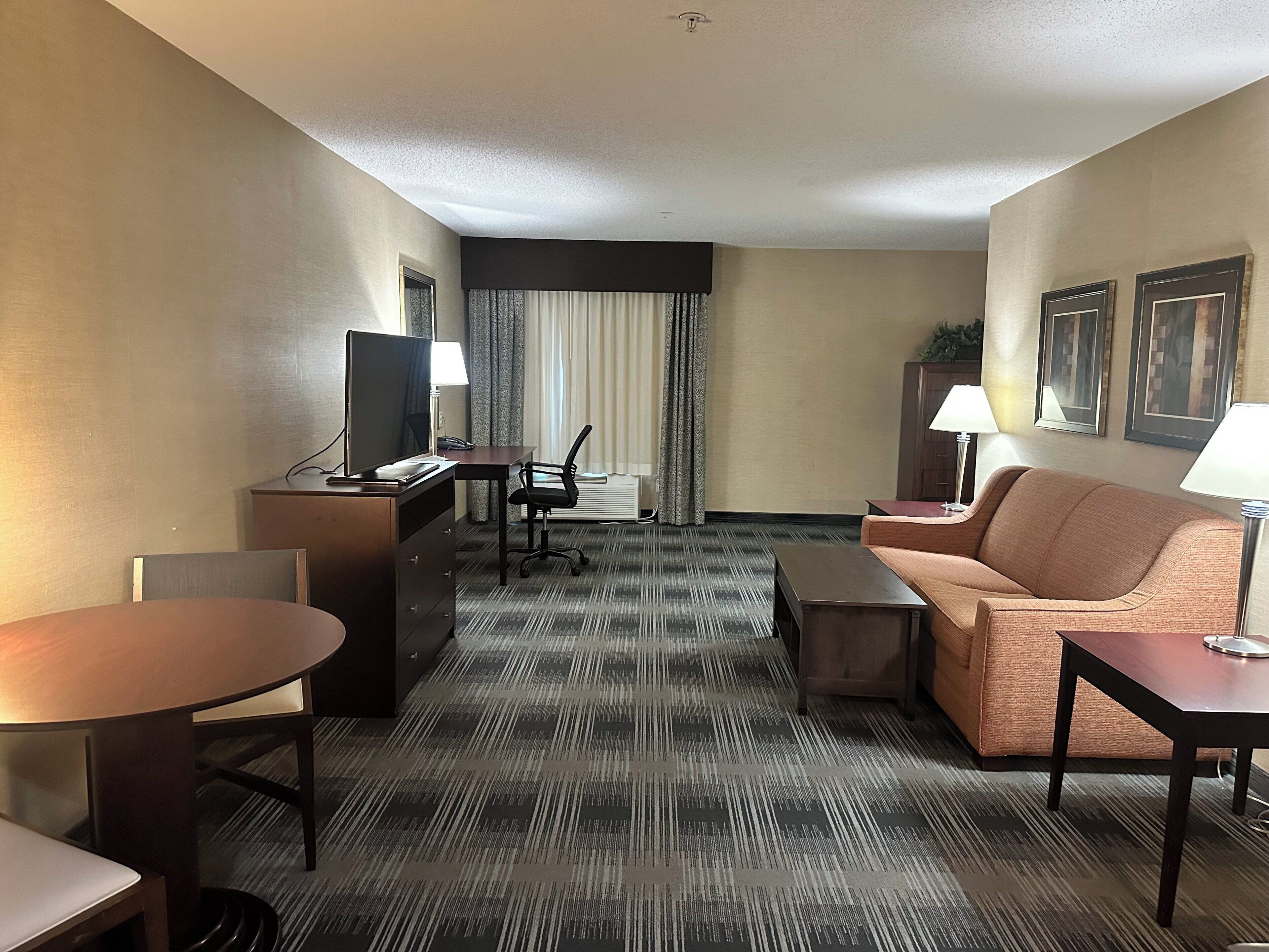 A hotel room with a bed, a desk with a computer, a chair, a sofa, and a small table.