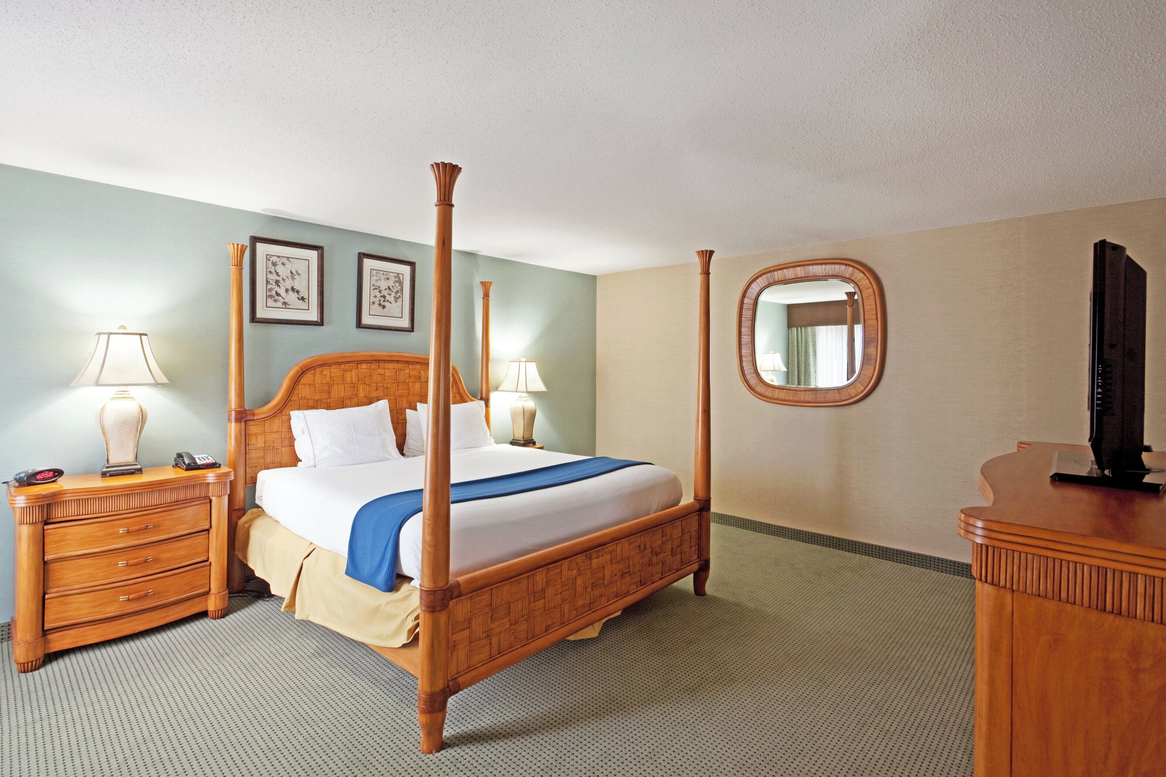 A hotel room with a four-poster bed, bedside tables, a mirror, and a television.