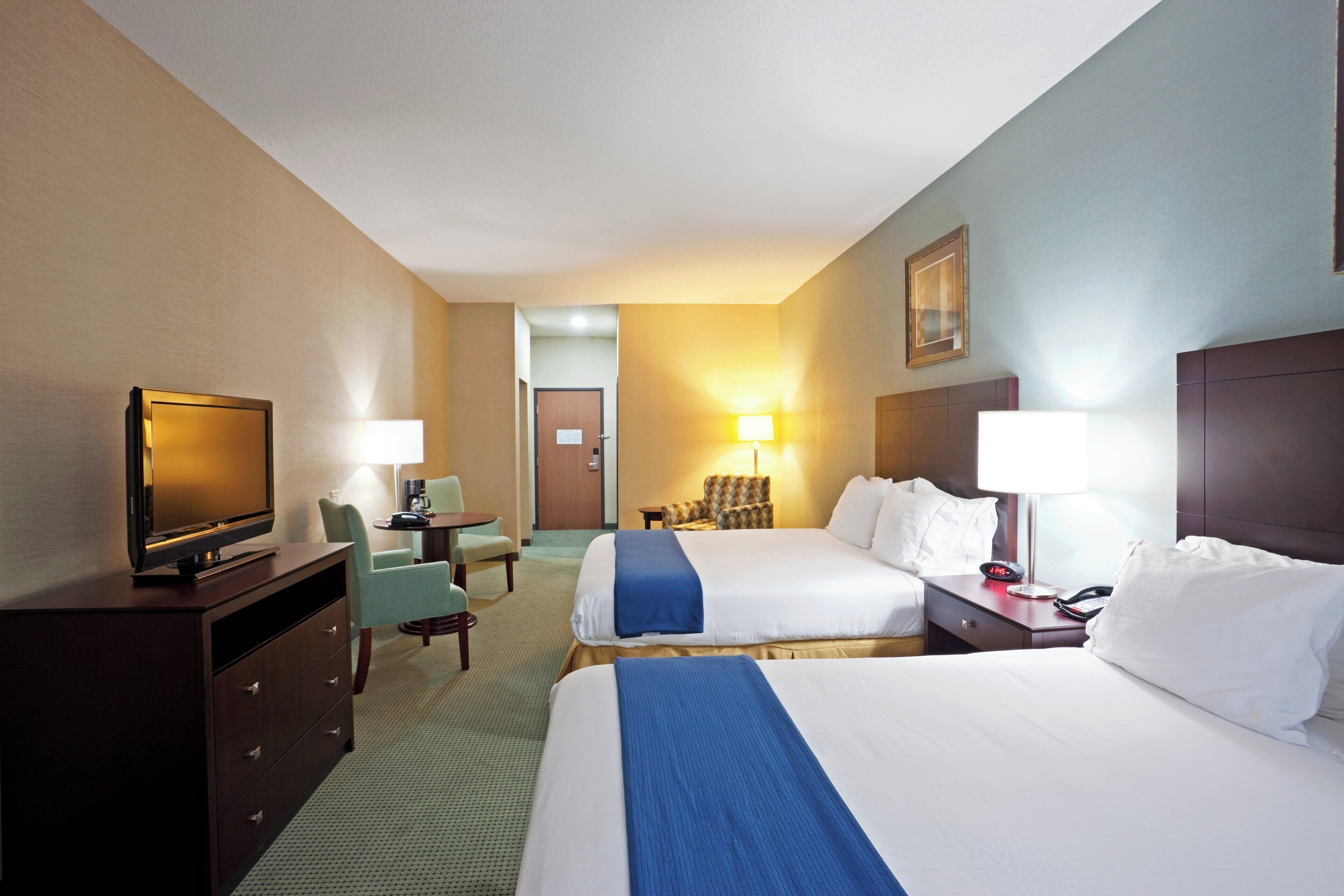 Ein Hotelzimmer mit zwei Betten, einem Schreibtisch mit Stuhl, einem Fernseher und einer Lampe.