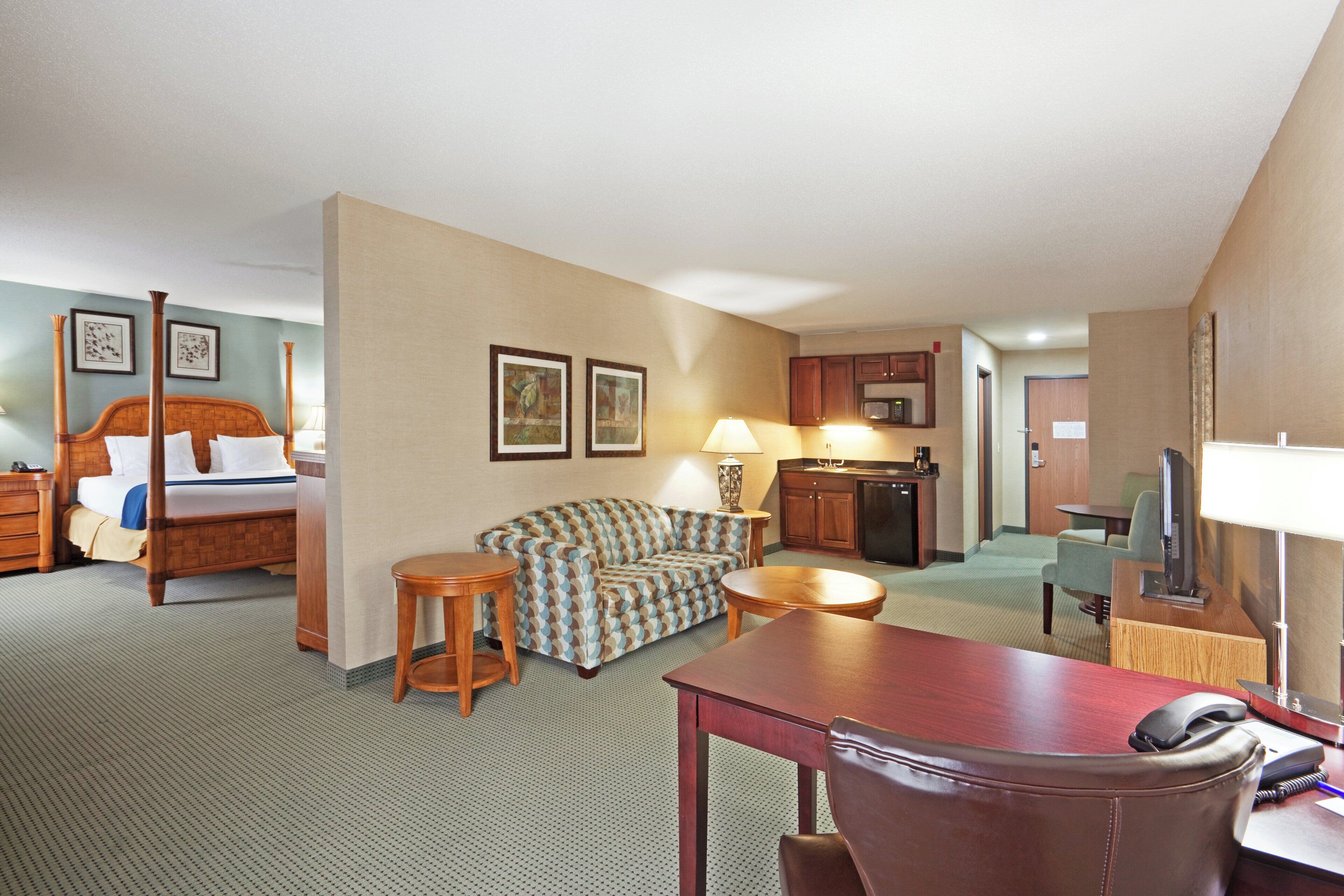 Habitación de hotel con cama, sofá, mesa de comedor, zona de cocina y televisión.