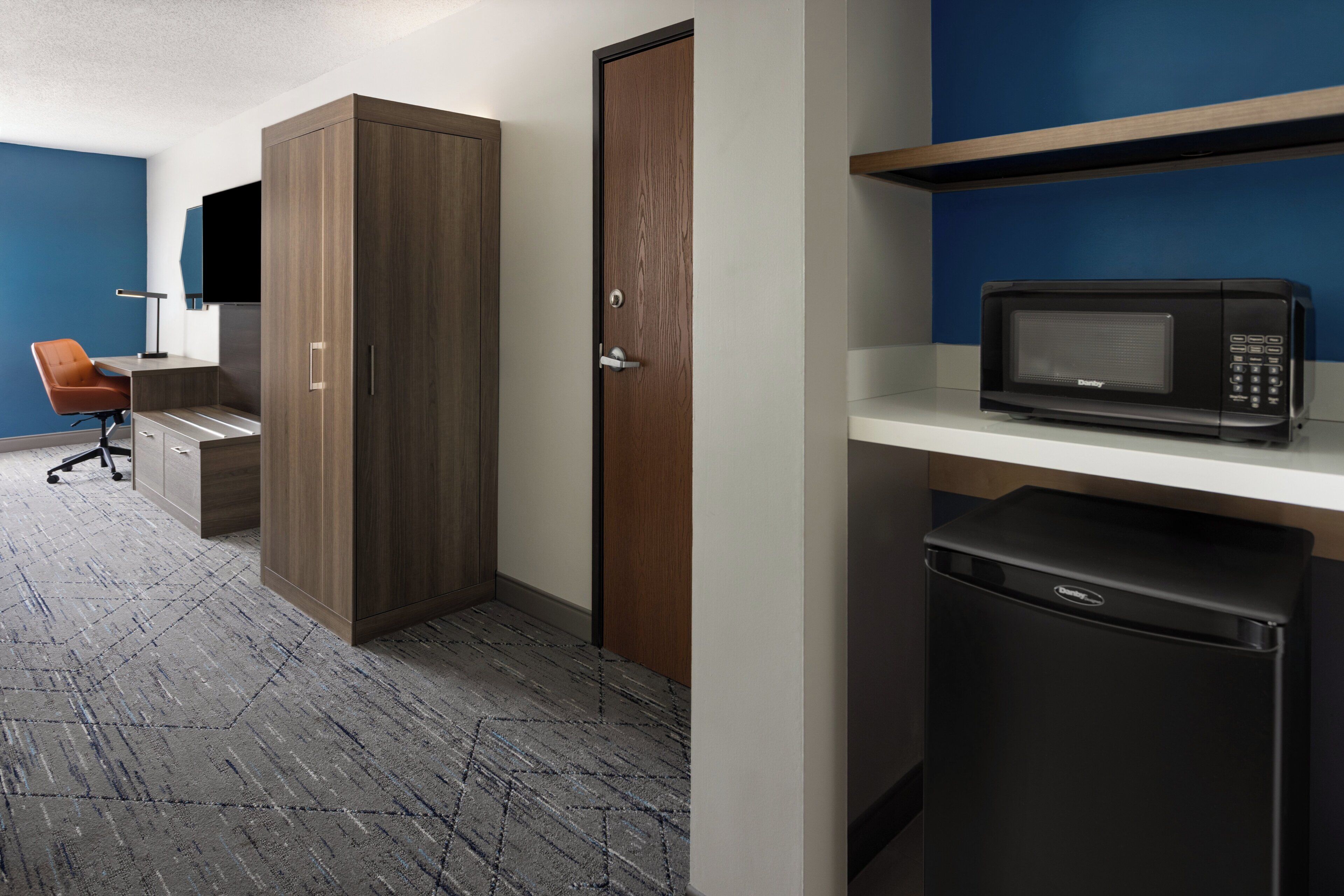 Een compacte hotelkamer met een kitchenette, een houten garderobe, een magnetron en een kleine koelkast.