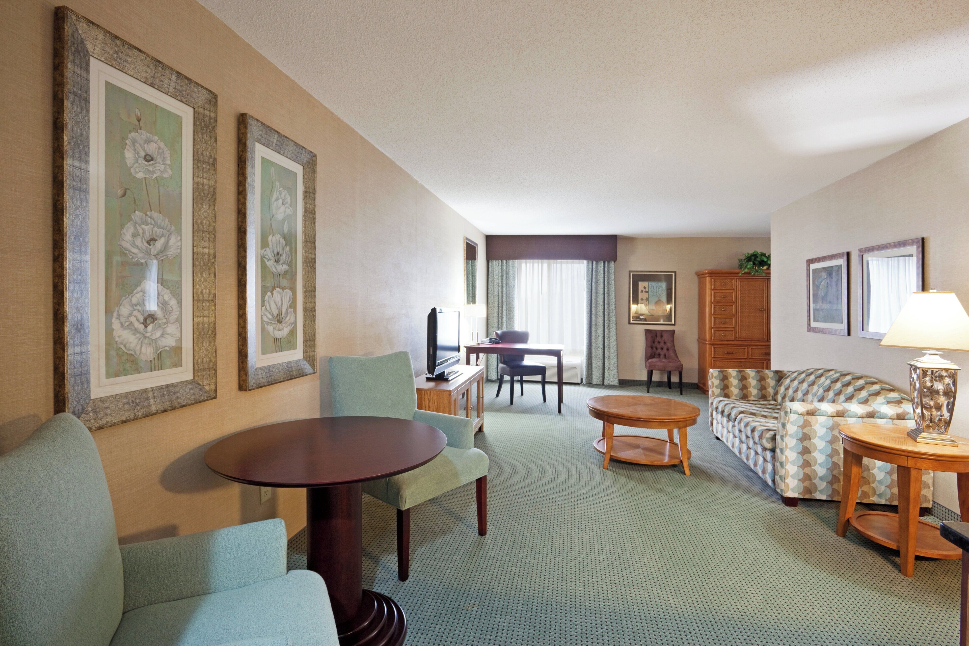 A hotel room with a dining area, a sofa, a small table, and a lamp.