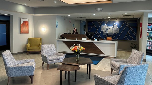 A hotel reception area with a modern design, featuring a reception desk, a seating area with armchairs, a coffee table, and a decorative vase with flowers. - Holiday Inn Express & Suites Meriden by IHG (Meriden)
