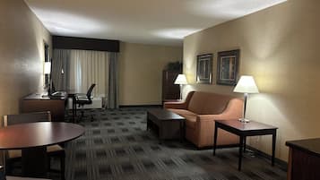 Ein Hotelzimmer mit Schreibtisch, Stuhl, Sofa, zwei Lampen und gerahmten Bildern an der Wand.