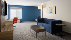 A modern hotel room with a blue accent wall, a sofa, a coffee table, a TV, and a lamp. - Holiday Inn Express & Suites Meriden by IHG (Meriden)