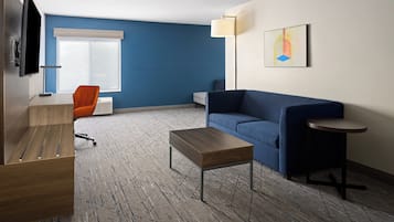 A modern hotel room with a blue accent wall, a sofa, a coffee table, a TV, and a lamp.