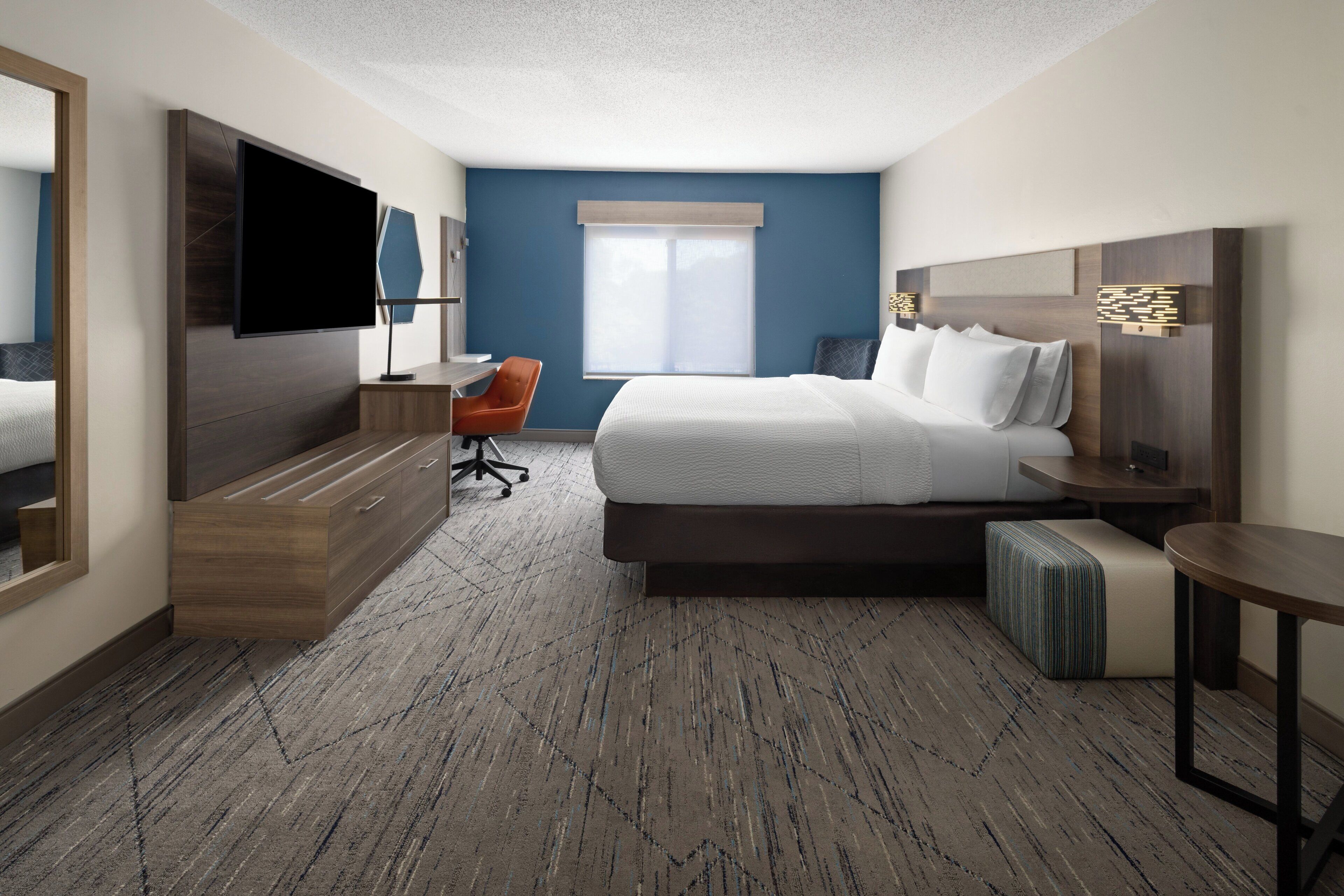A hotel room with a large bed, a desk, a chair, a TV, and a window with blinds.