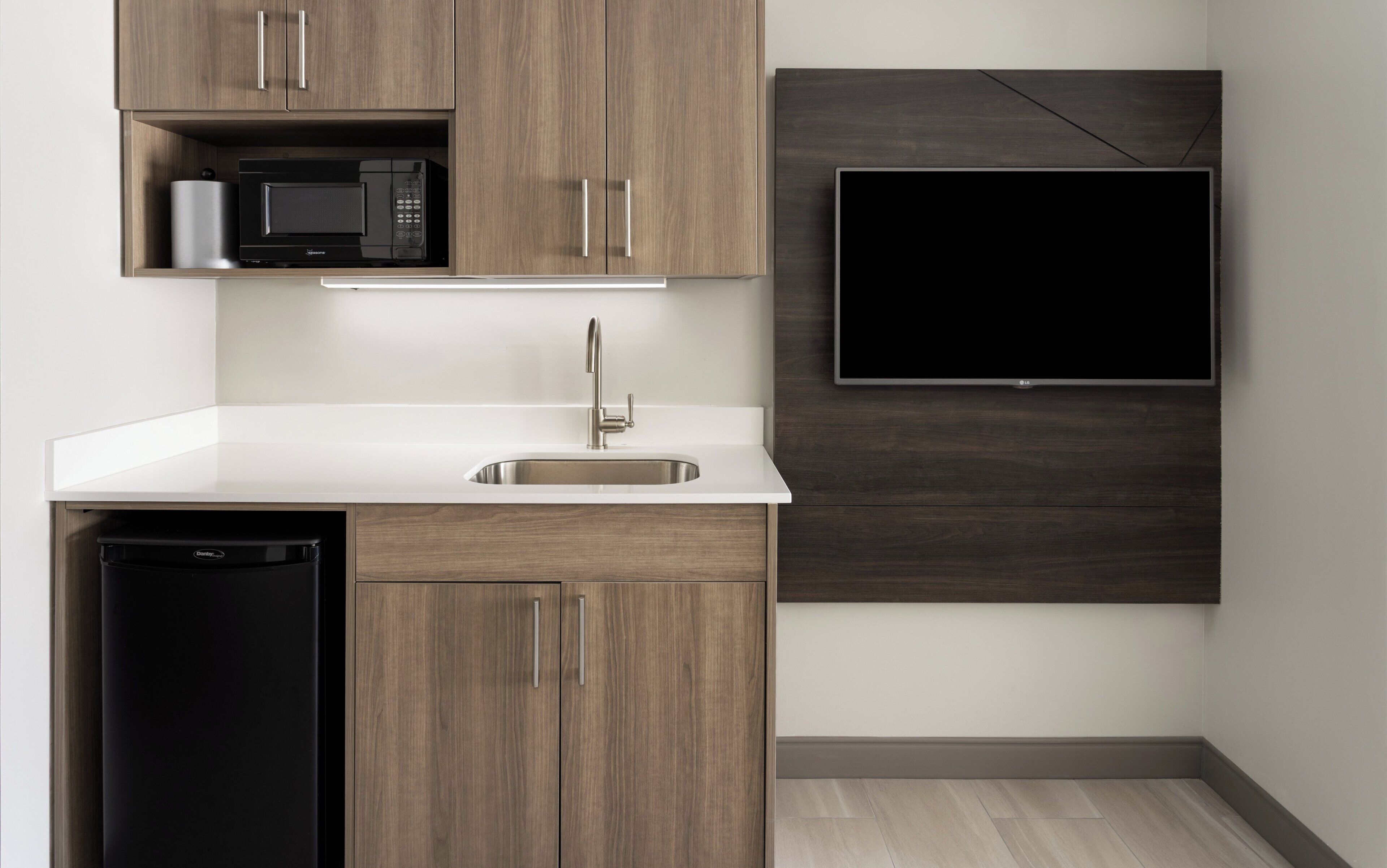 A modern kitchen with a built-in microwave, a sink, and a flat-screen TV mounted on the wall.