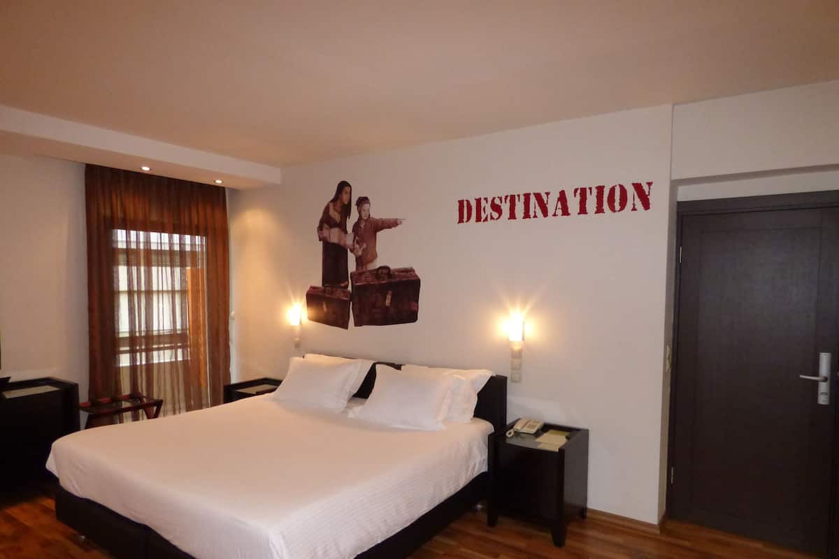 Une chambre d’hôtel avec un grand lit, deux tables de chevet, une œuvre d’art accrochée au mur et une porte.