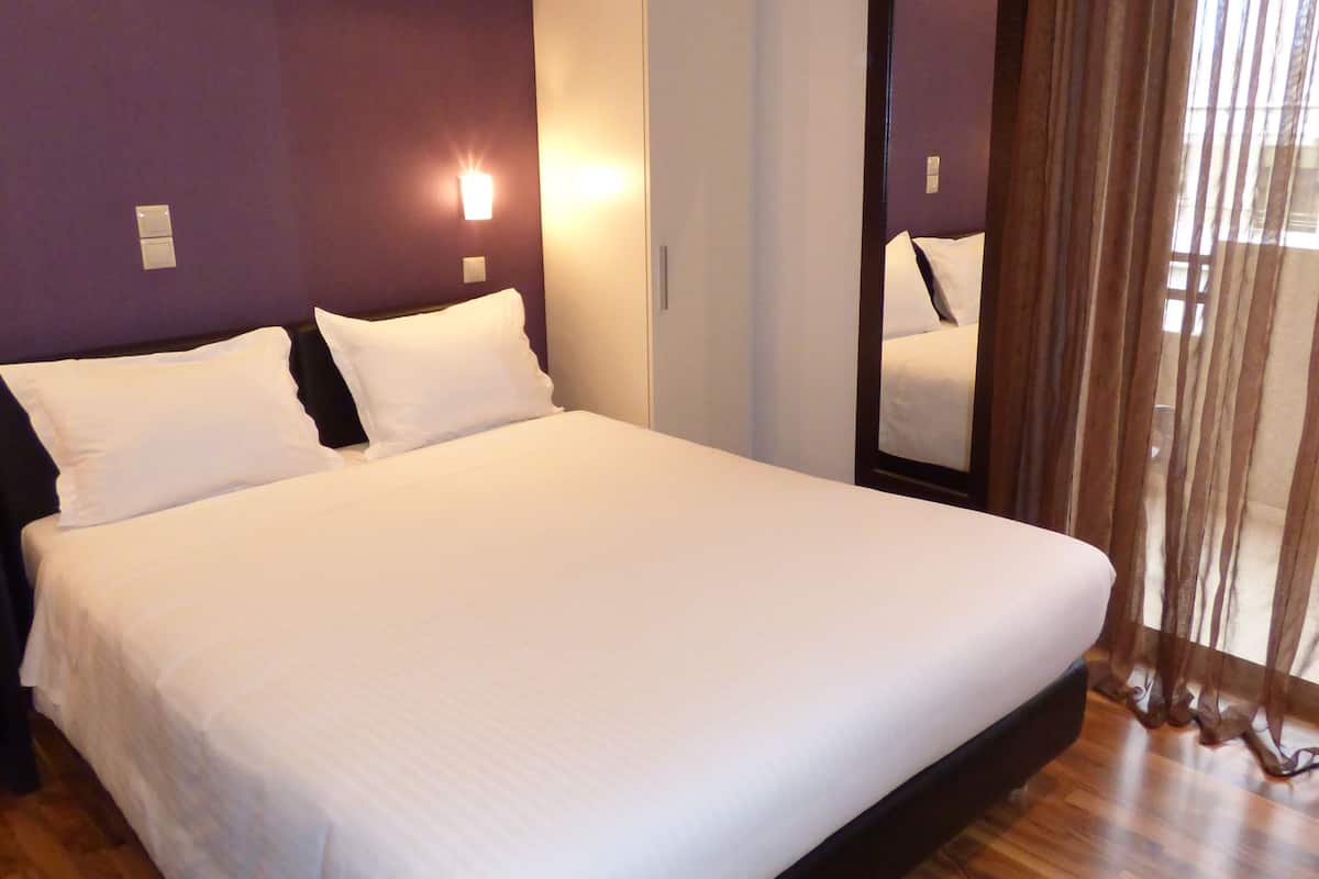 Un grand lit avec du linge de lit blanc, une tête de lit sombre et un plancher en bois.