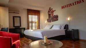 A hotel room with a bed, a red chair, a round table with a candle, a wall-mounted TV, and a 'DESTINATION' sign. - Athens Habitat (Marousi)