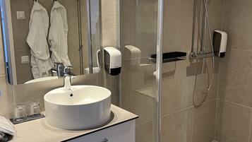 A modern bathroom with a large mirror, a round sink, a glass shower enclosure, and a toilet.