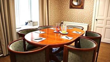 A conference room with a round wooden table, six upholstered chairs, and a decorative mirror on the wall.
