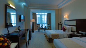 A hotel room with two beds, a desk with a lamp, a TV, and a view of the city through large windows. - Harmony Hotel (Addis Ababa)