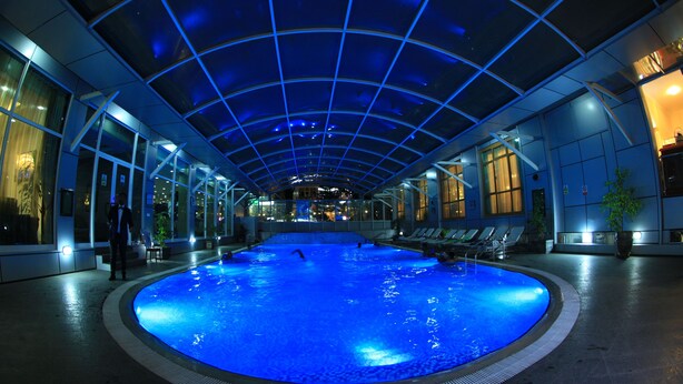An indoor swimming pool with a glass ceiling, surrounded by lounge chairs and potted plants. - Harmony Hotel (Addis Ababa)