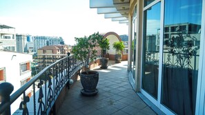 Un balcón con plantas en macetas, una puerta de cristal y vistas a la ciudad.
