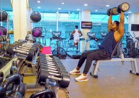 Academia com equipamentos de ginástica, esteiras e uma pessoa usando um banco de musculação.