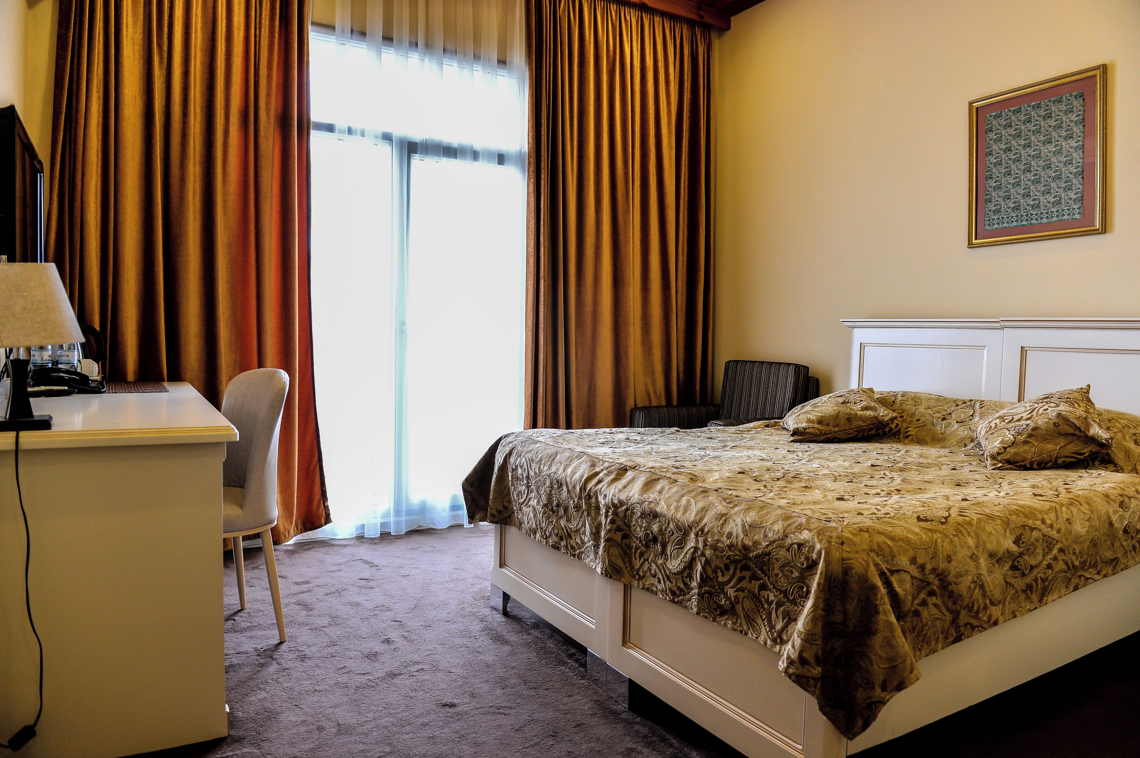 Habitació d'hotel amb llit, escriptori, cadira i finestra amb cortines.
