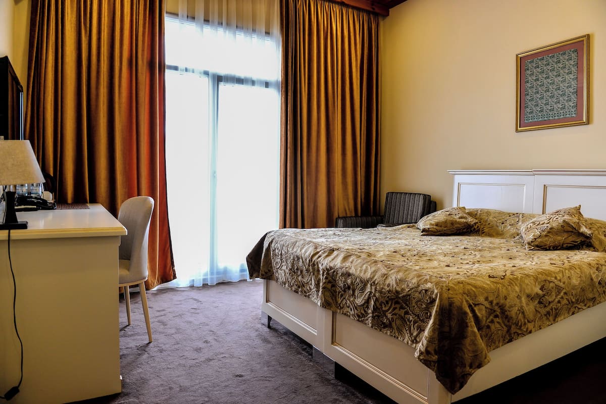 Une chambre d’hôtel avec un lit, un bureau, une chaise et une fenêtre avec des rideaux.
