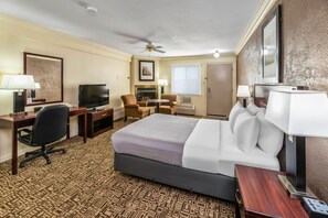 A hotel room with a bed, desk, chair, television, and a fireplace.