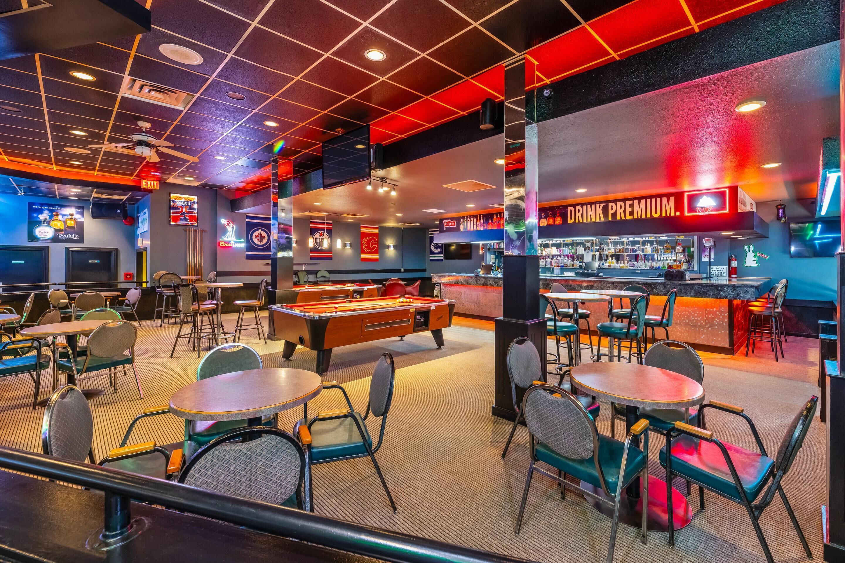 Una sala de billar con mesas, sillas y una mesa de pool.