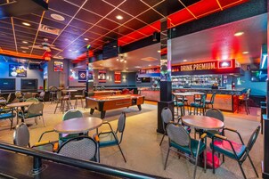 Una sala de billar con mesas, sillas y una mesa de pool.