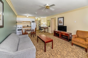 A living room with a sofa, a patterned carpet, a wooden coffee table, a TV stand, and a ceiling fan. - Quality Inn & Suites (High Level)