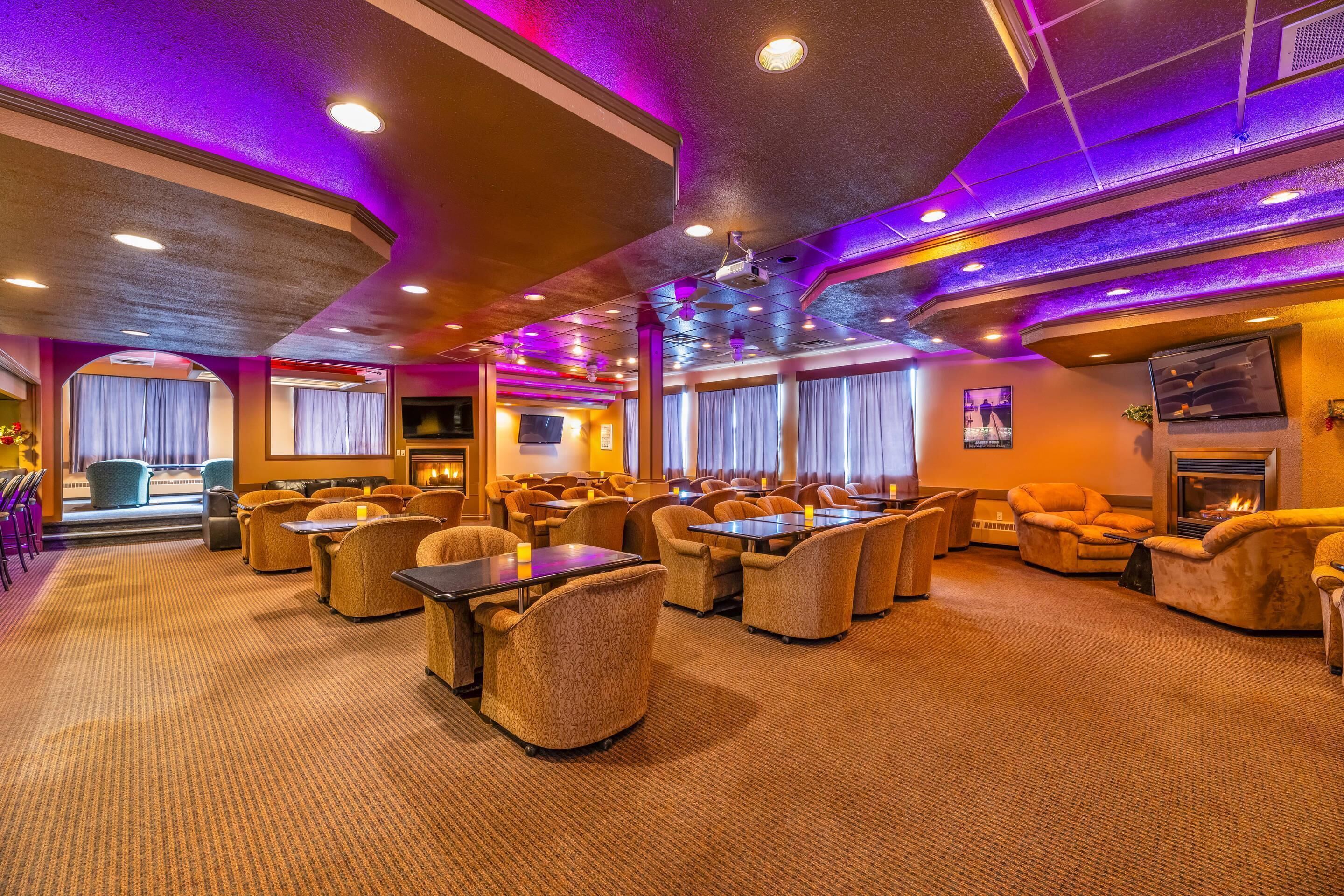 A spacious hotel lobby with multiple seating areas, a fireplace, and a large window with curtains.