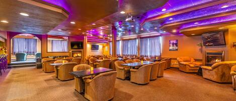 A spacious hotel lobby with multiple seating areas, a fireplace, and a large window with curtains.