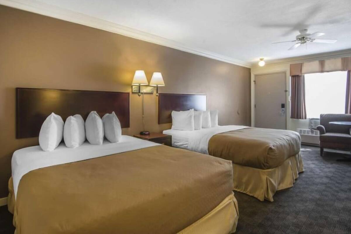 Quarto de hotel com duas camas, um ventilador de teto e uma janela com cortinas.