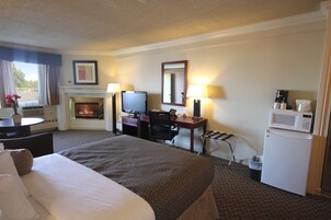 A hotel room with a bed, desk, chair, television, fireplace, and a microwave.