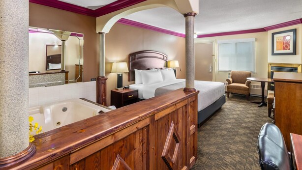 A hotel room with a large bed, a sitting area with a chair and table, a bathroom with a bathtub, and a desk with a chair.