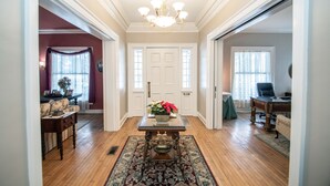 A spacious living room with hardwood floors, a chandelier, a dining table with a vase of flowers, and a sofa. - Looking Glass Inn (Indianapolis)
