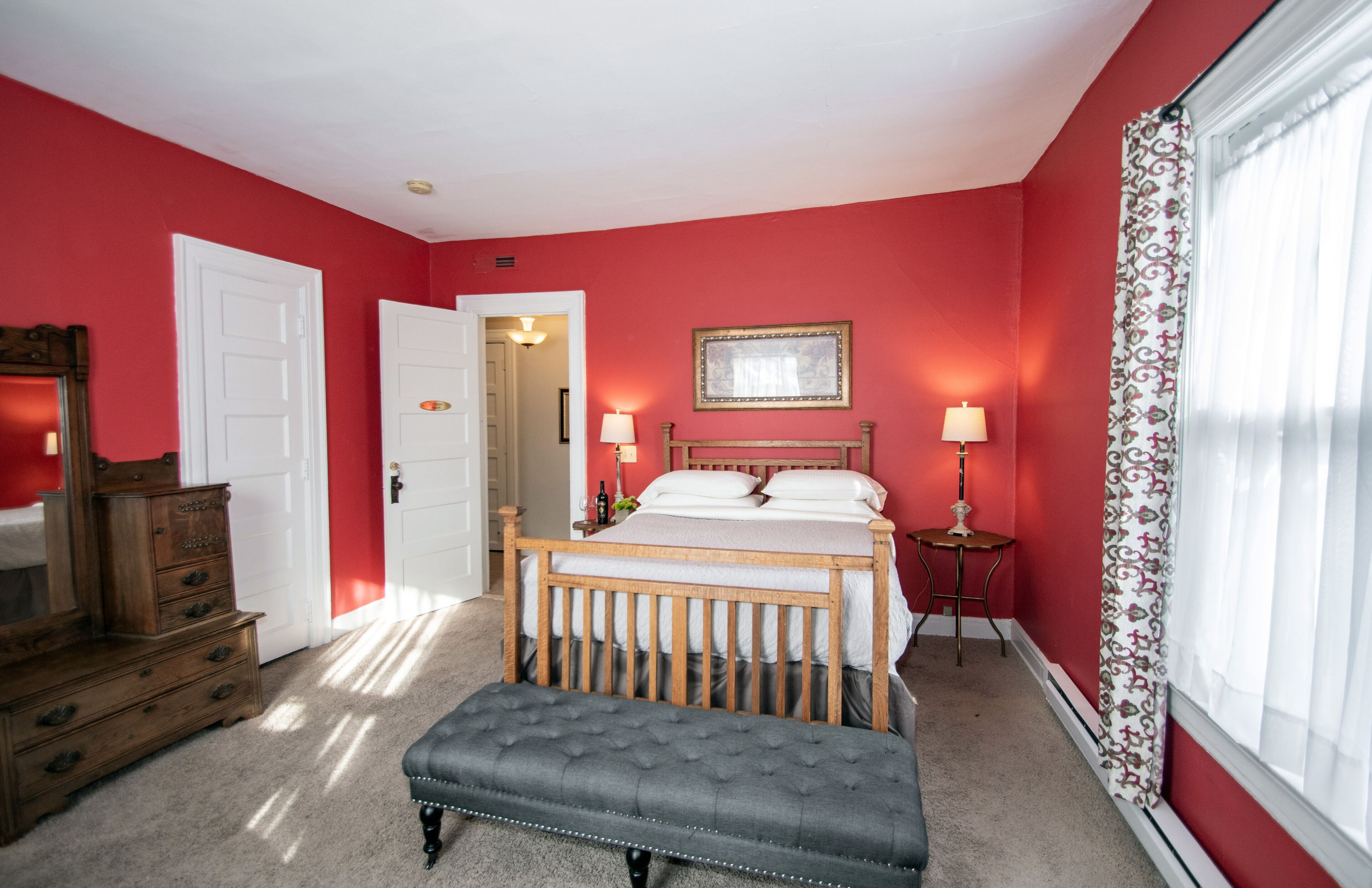A bedroom with a wooden bed, a bench, a dresser, and a mirror.