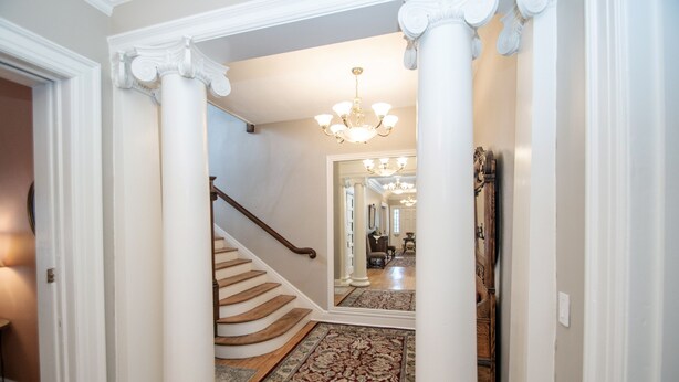 A grand staircase with a wooden handrail, a patterned rug, and a chandelier. - Looking Glass Inn (Indianapolis)