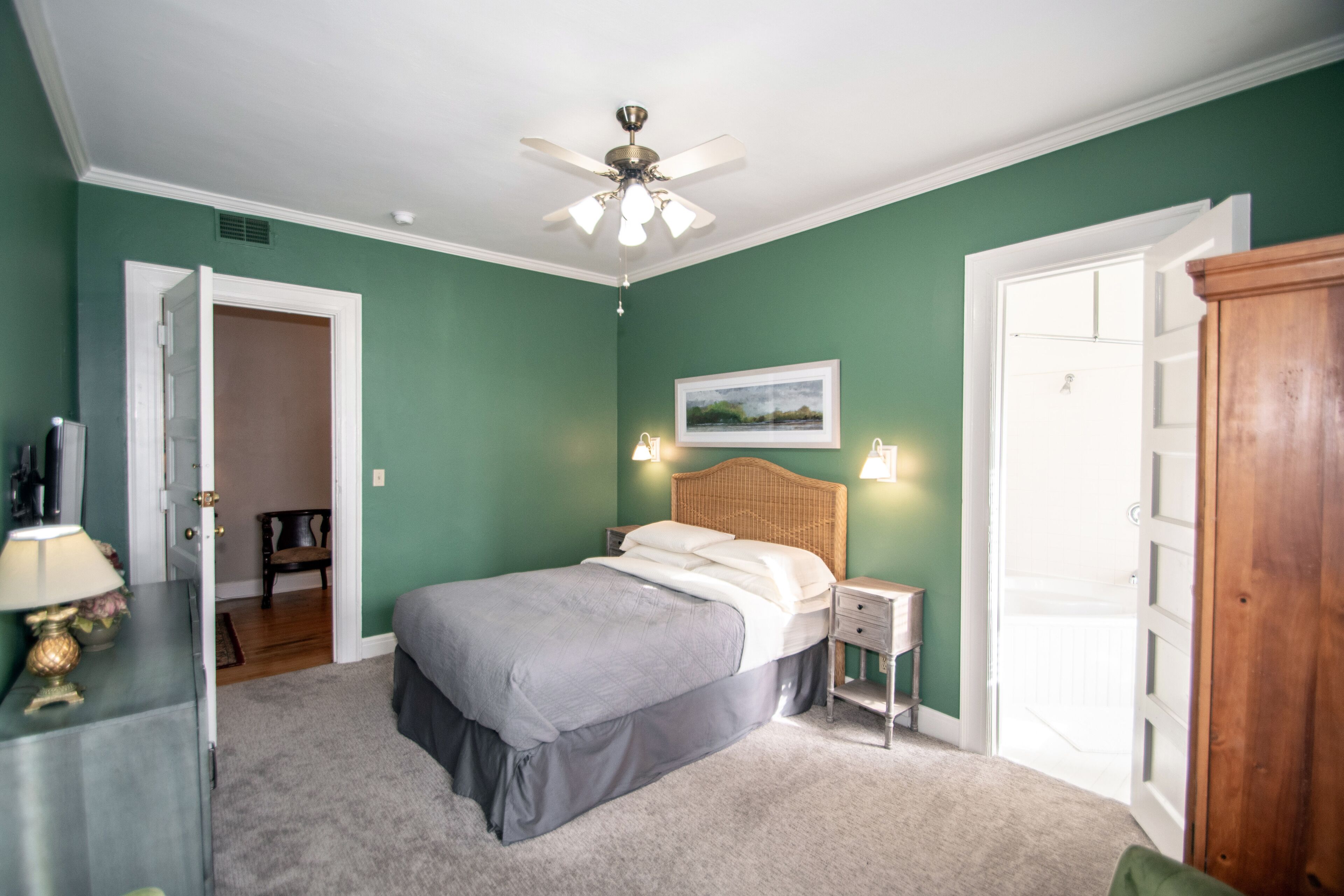 Ein Schlafzimmer mit einem Bett, Nachttischen, einem Deckenventilator und einer Tür zu einem anderen Raum.
