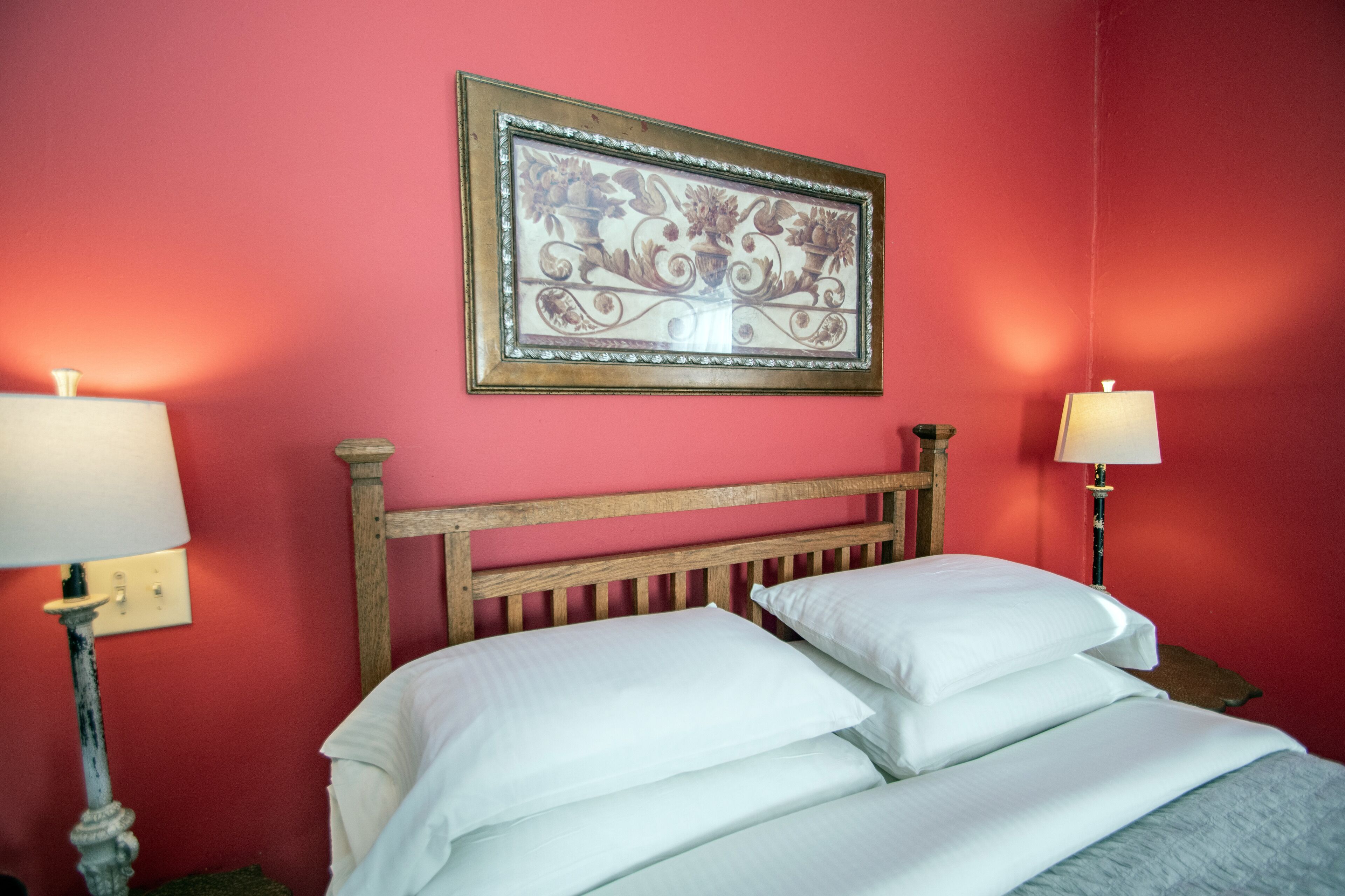 A room with a bed, two bedside lamps, and a framed artwork on the wall.