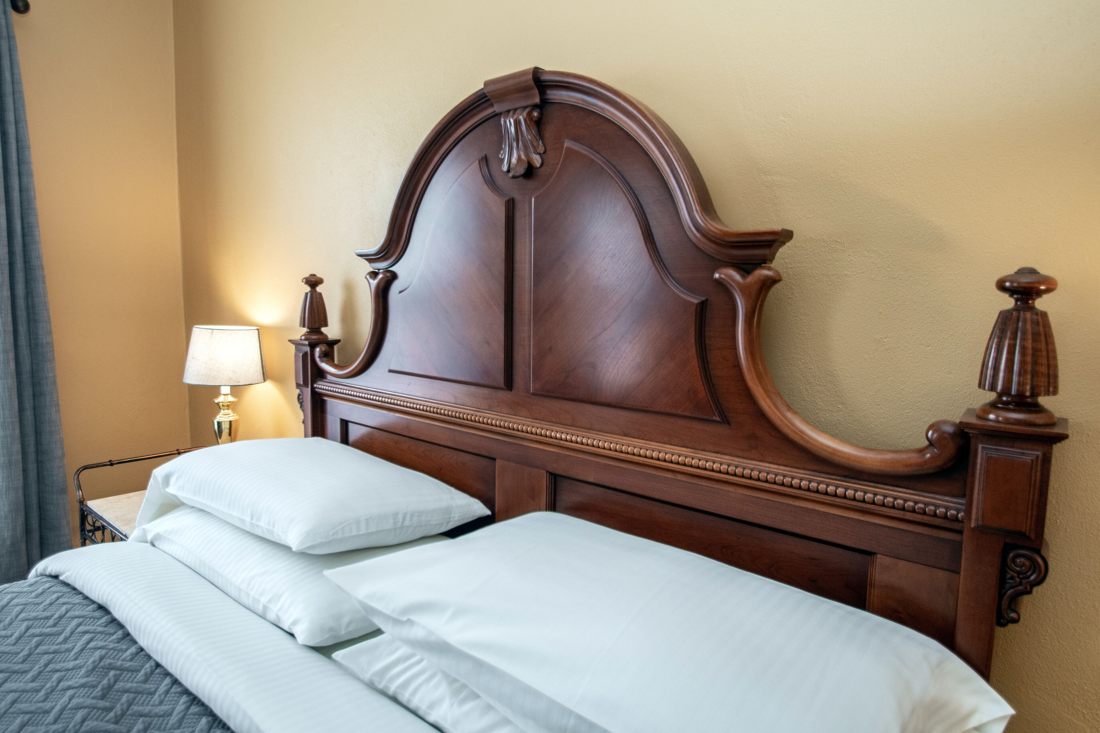 A neatly made bed with a wooden headboard, a bedside lamp, and a wall lamp.