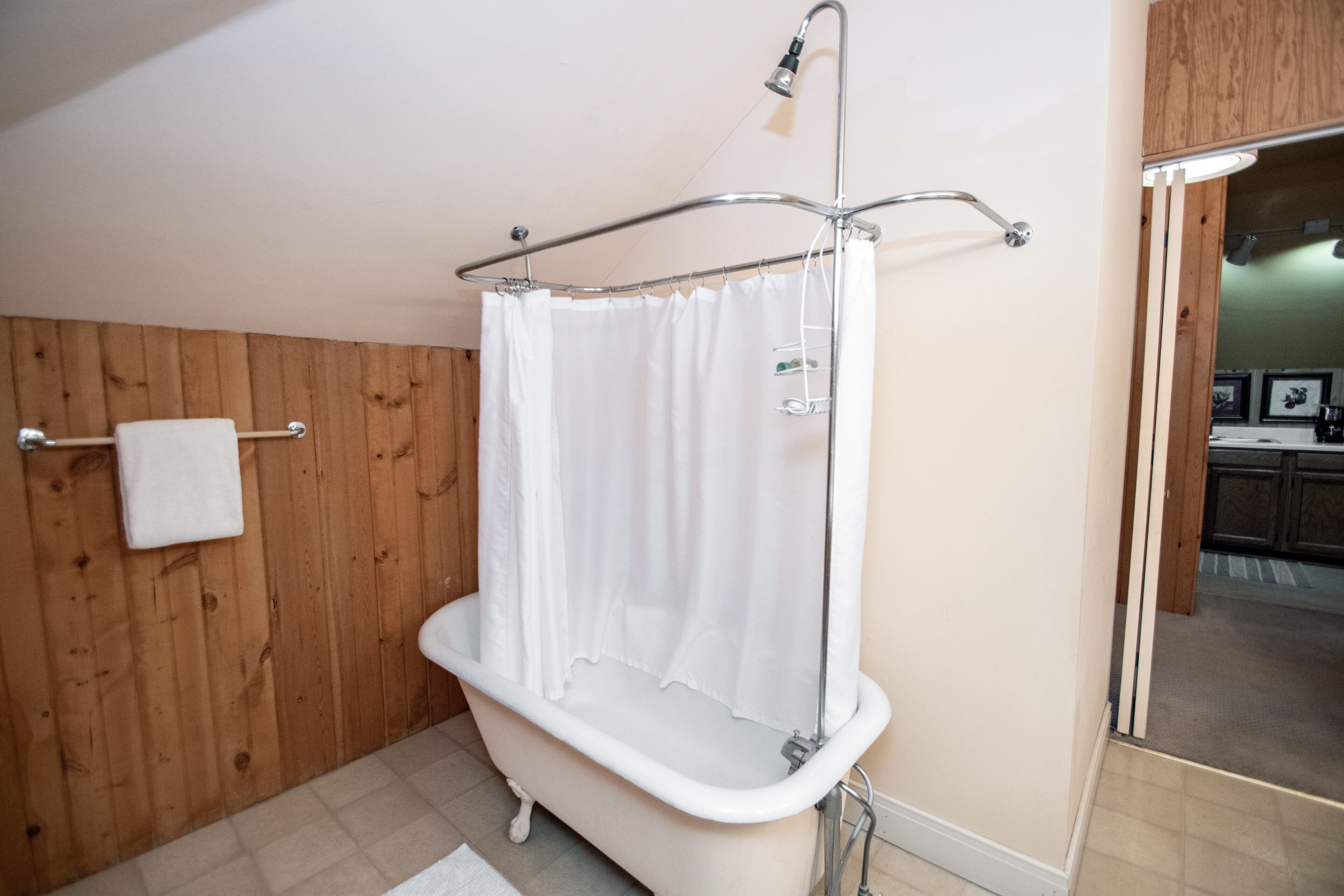 Een badkamer met een pootbad, een houten wand, een witte handdoek en een douchegordijn.