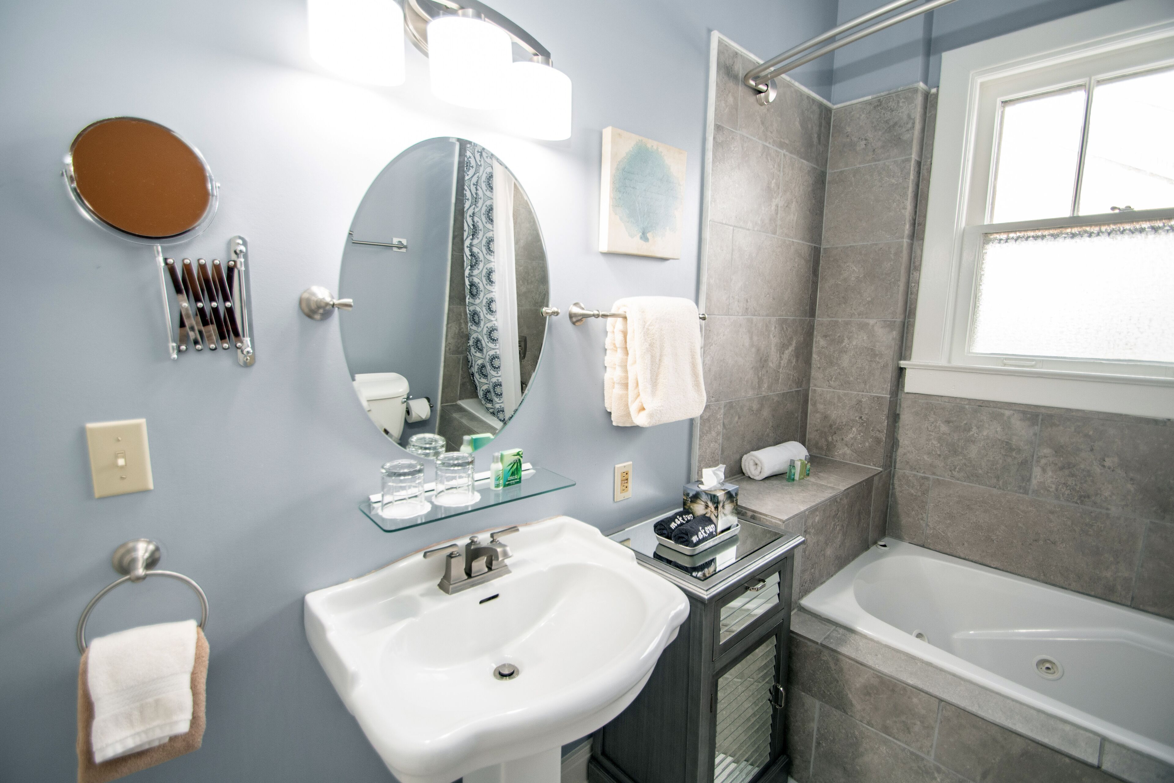 A modern bathroom with a white sink, a round mirror, a glass shower enclosure, and a bathtub.
